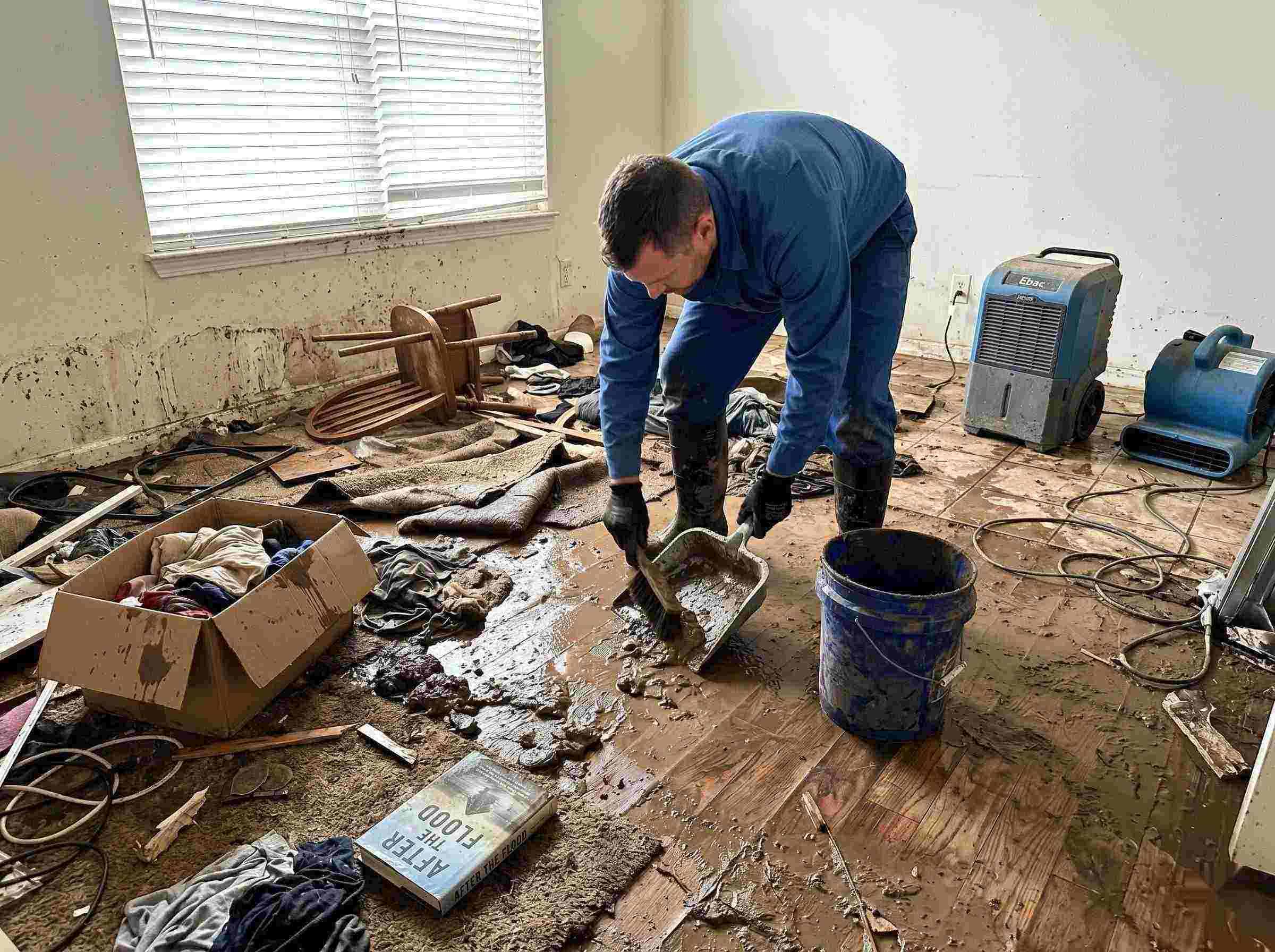 Realistic photo of a technician performing mud and debris removal after a home flood in Salt Lake City, showing soaked furniture, wet flooring, and scattered debris during post-flood cleanup.